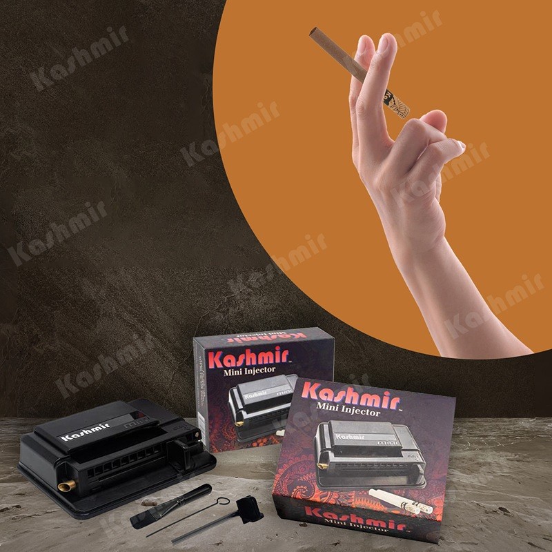 Hand holding a Kashmir Bronze Brown cigarette tube above a Kashmir Mini Injector with two boxed units and included tools on a stone surface.