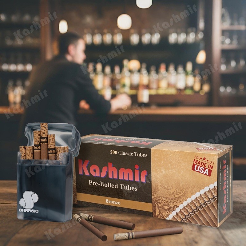 Kashmir Bronze pre-rolled tubes, 200-count carton with brown tubes and an open pocket case on a bar counter; Made in USA badge visible.