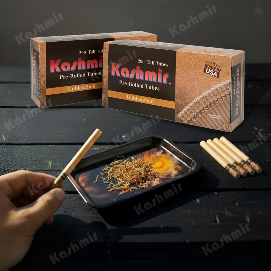 Hand filling a natural Kashmir Unbleached tall pre-rolled tube over a tray, with two 200-count cartons in the background and spare tubes on the table.