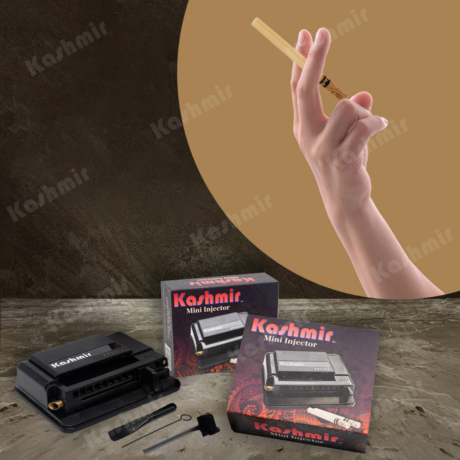 Hand holding a natural unbleached Kashmir tall pre-rolled tube above a Kashmir Mini Injector with two product boxes and injector tools on a stone surface.